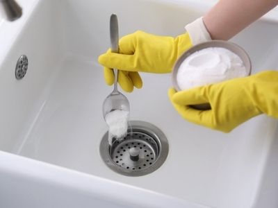 Person using a spoon to put baking soda down a drain