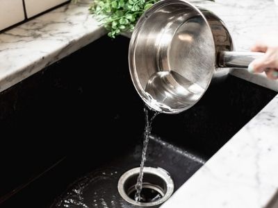 Boiler water being poured down the drain of a kitchen sink