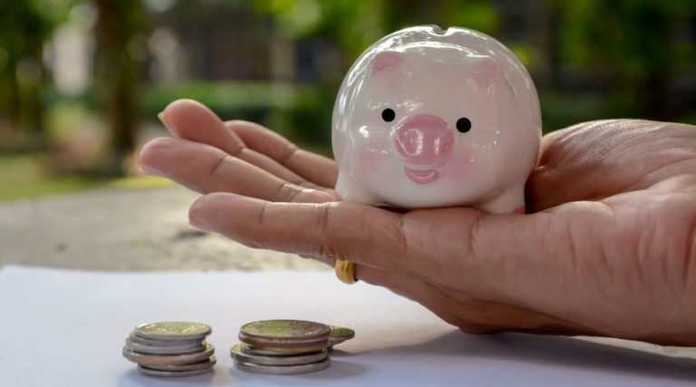 Small piggy bank in a hand with coins next to it