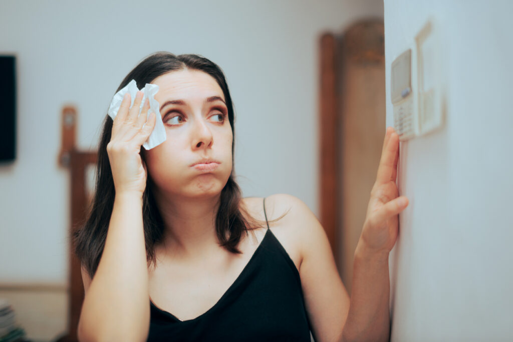 woman in black shirt sweating and adjusting temperature on home thermostat